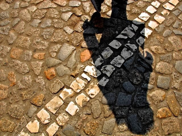 A cobblestone street with a double white line and a person's shadow crossing the line - cross the line concept